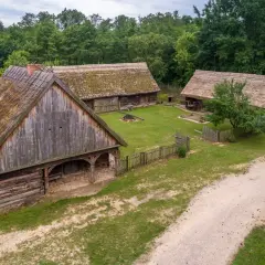 Drewniane chaty ze słomianymi dachami w skansenie, otoczone zielenią.