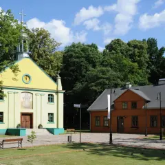 Żółty kościółek i pomarańczowy dom drewniany na tle zieleni i błękitnego nieba.