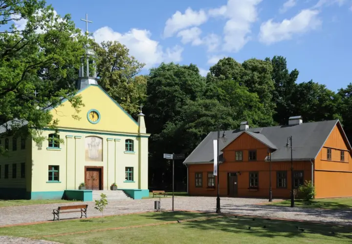 Żółty kościółek i pomarańczowy dom drewniany na tle zieleni i błękitnego nieba.